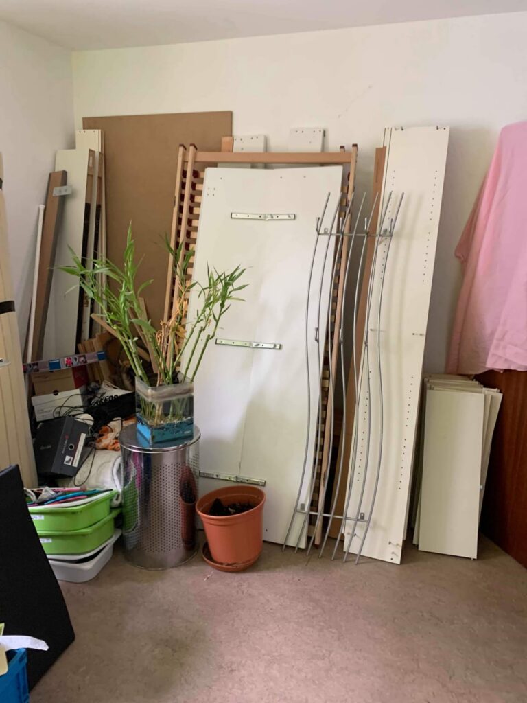Zimmer mit gelagerten Lattenrosten, Platten und Hausrat vor der Entrümpelung