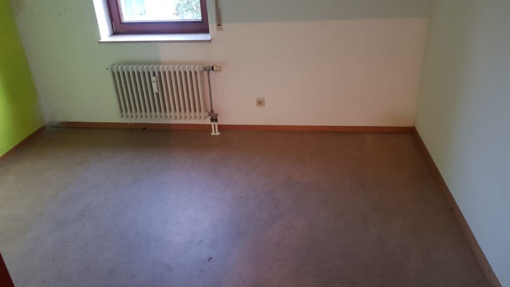 Leeres Zimmer mit grüner Wand und Heizkörper nach der Entrümpelung